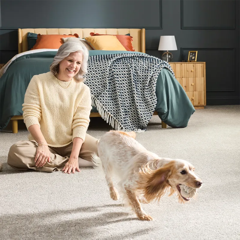 Women in bedroom playing with her dog on the carpeted floor
